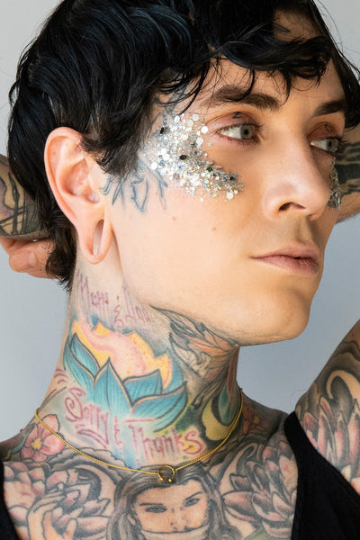 Tattooed model wearing a gold choker with barbell pendant and delicate gold chain.