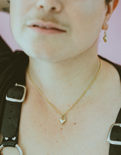 Close-up of gold heart charm choker on model wearing black leather harness