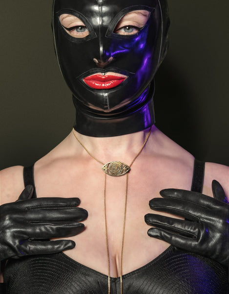 Model wearing gold bolo tie, black latex mask, black gloves and black bullet bra