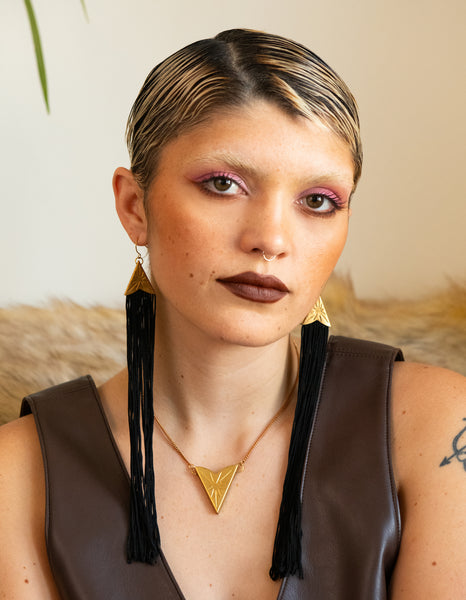 Model wearing long black tassel earrings with sunburst cap, matching choker and brown pleather dress