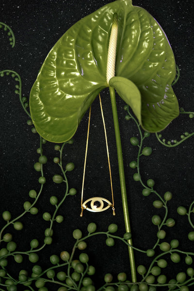Black resin eye choker on a black background, surrounded by plants