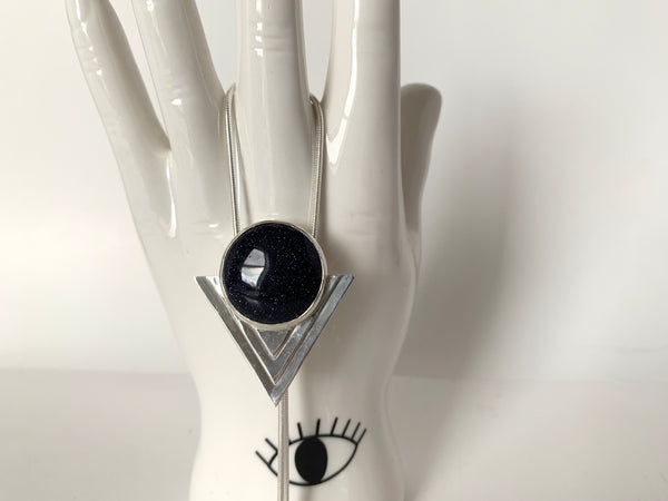 Close-up of blue goldstone and sterling silver pendant of the bolo tie hanging from a ceramic hand