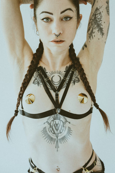 Model wearing black harness and conical gold metal nipple pasties