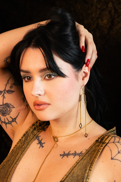 Model wearing geometric brass dangle earrings and a browm denim top