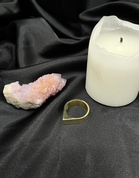 Pointed brass ring on a black silk background with a white candle and pink quartz crystal