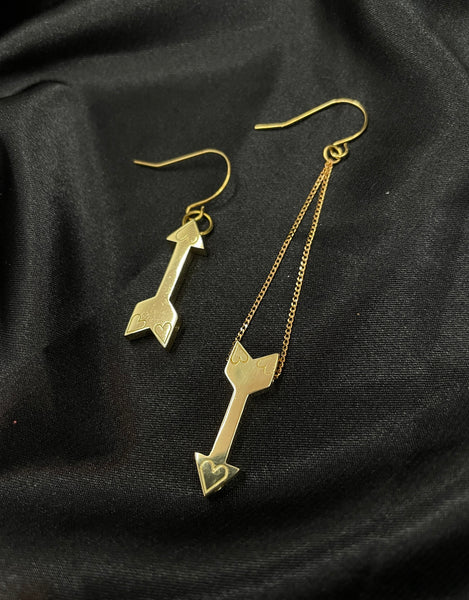 Gold arrow earrings on a black silk background