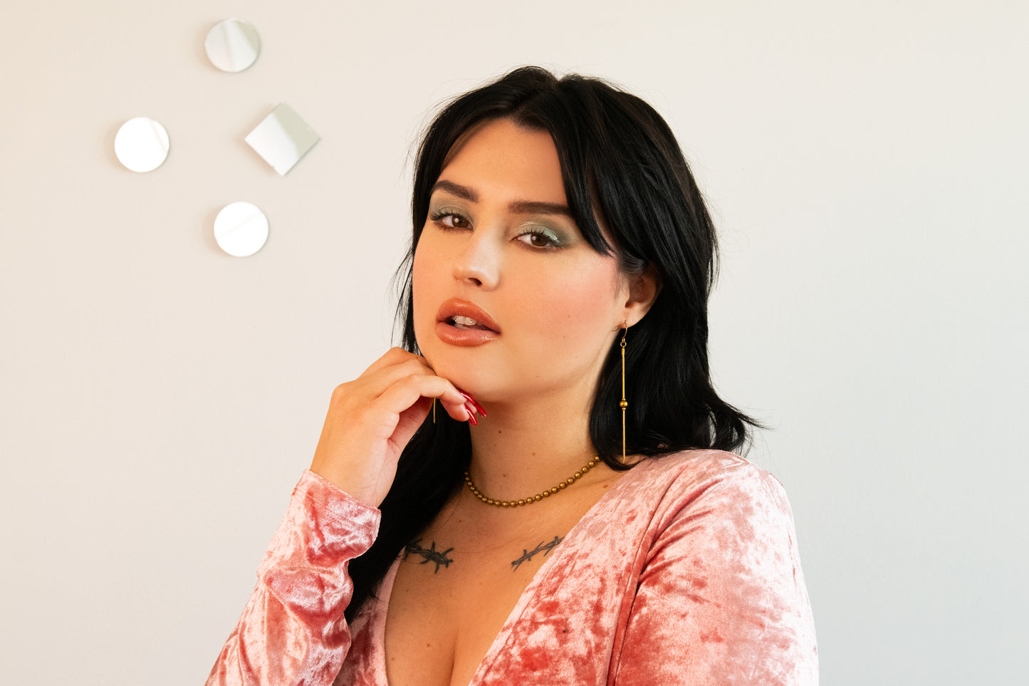 Model wearing gold drop earrings, ball chain choker and pink velvet top
