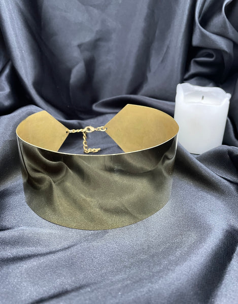 Gold choker necklace and a candle on a black silk background