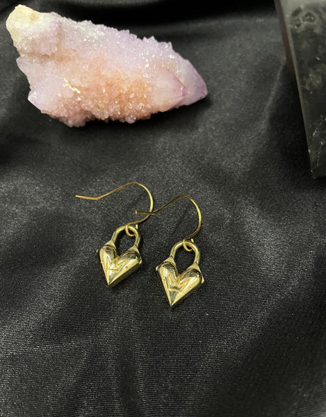 Close-up of back of heart charm earrings with crown logo on a black silk background