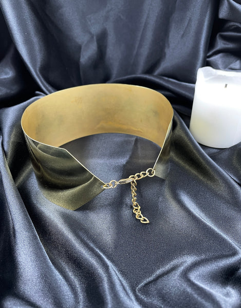 Clasp closure of back of thick gold band choker on a black silk background and a white candle