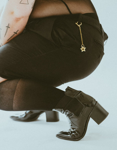 Close-up of model crouching, wearing black shorts, socks and boots with spur keychain on belt loop