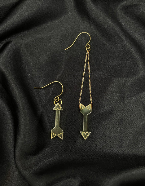 Mismatch gold arrow earring with engraved hearts on a black silk background