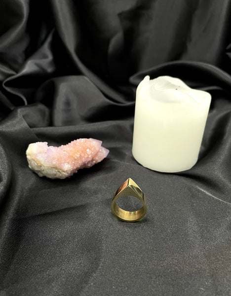 Gold pointed ring on edge on a black silk background, white candle and pink quartz crystal