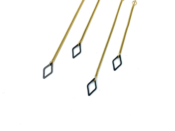 Close-up of black diamond charms and foxtail snake chain of dangle earrings on a white background