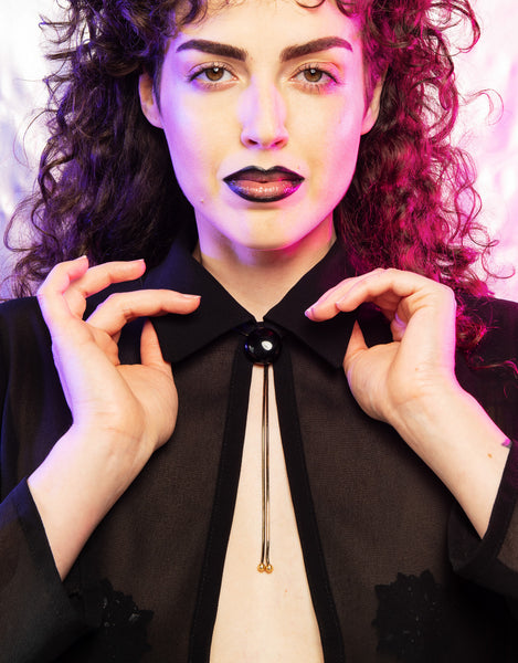 Model wearing onyx bolo tie and translucent black collared top
