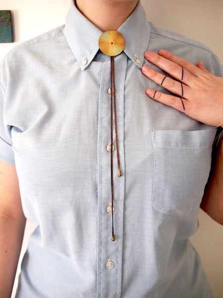 Bolo tie necklace worn under a blue collared shirt