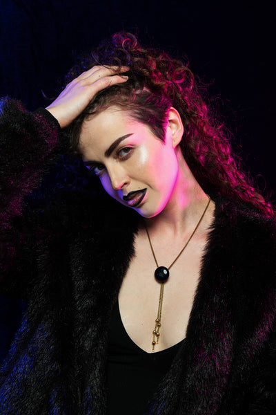 Model wearing blue goldstone bolo tie cinched midway, faux fur coat, holding her hair back