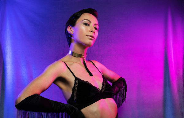 Model wearing gold choker with tassel, black velvet bralette and black tassel gloves