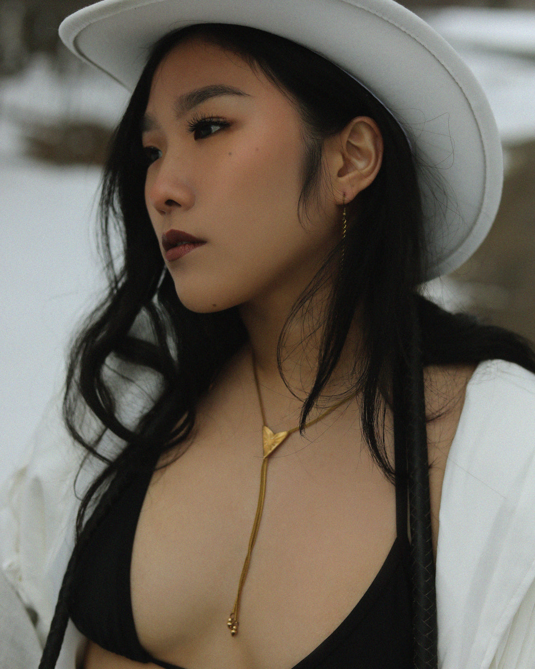 Queer in a white cowboy hat, bolo tie, black bra and white tassel leather jacket