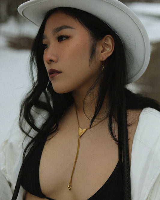 Queer in a white cowboy hat, bolo tie, black bra and white tassel leather jacket