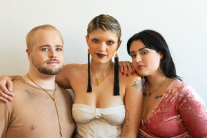 Three models embrace each other while wearing a brass bolos, tassel earrings and a star choker.