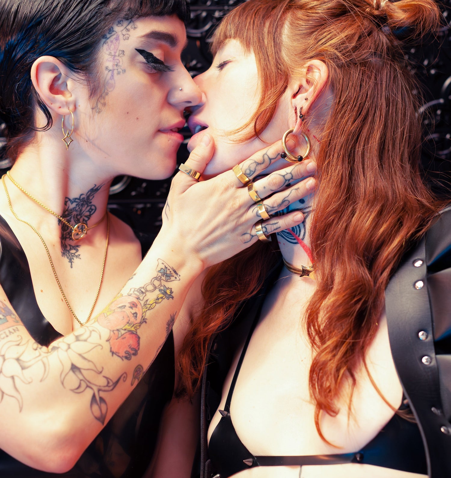 Two models about to kiss, wearing black latex and gold rings