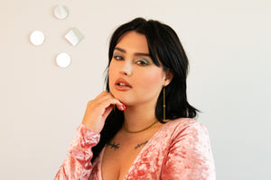 Model wears a pink velvet shirt, gold drop earrings and a ball chain choker