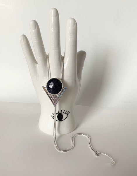 A blue goldstone bolo tie hangs from a white ceramic hand in front of a white background