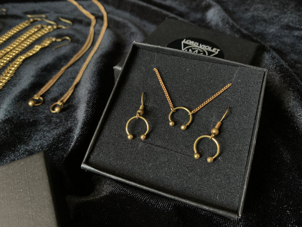 Gold barbell choker and earrings in a black gift box on a black velvet background