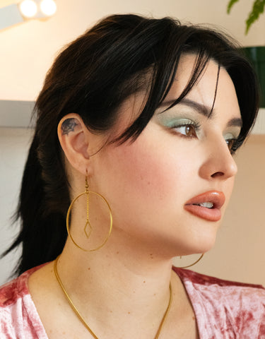 Side view of model wearing big hoop earrings with dangling charm