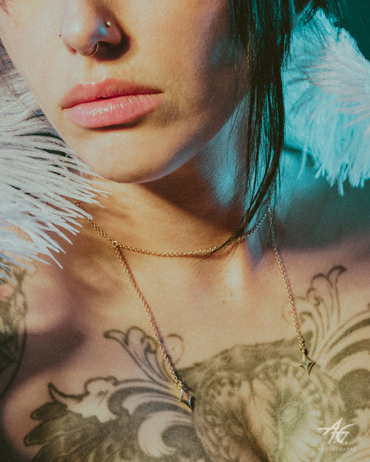 Close-up of model wearing a delicate gold chain necklace with star charms, teal lighting and white feathers.