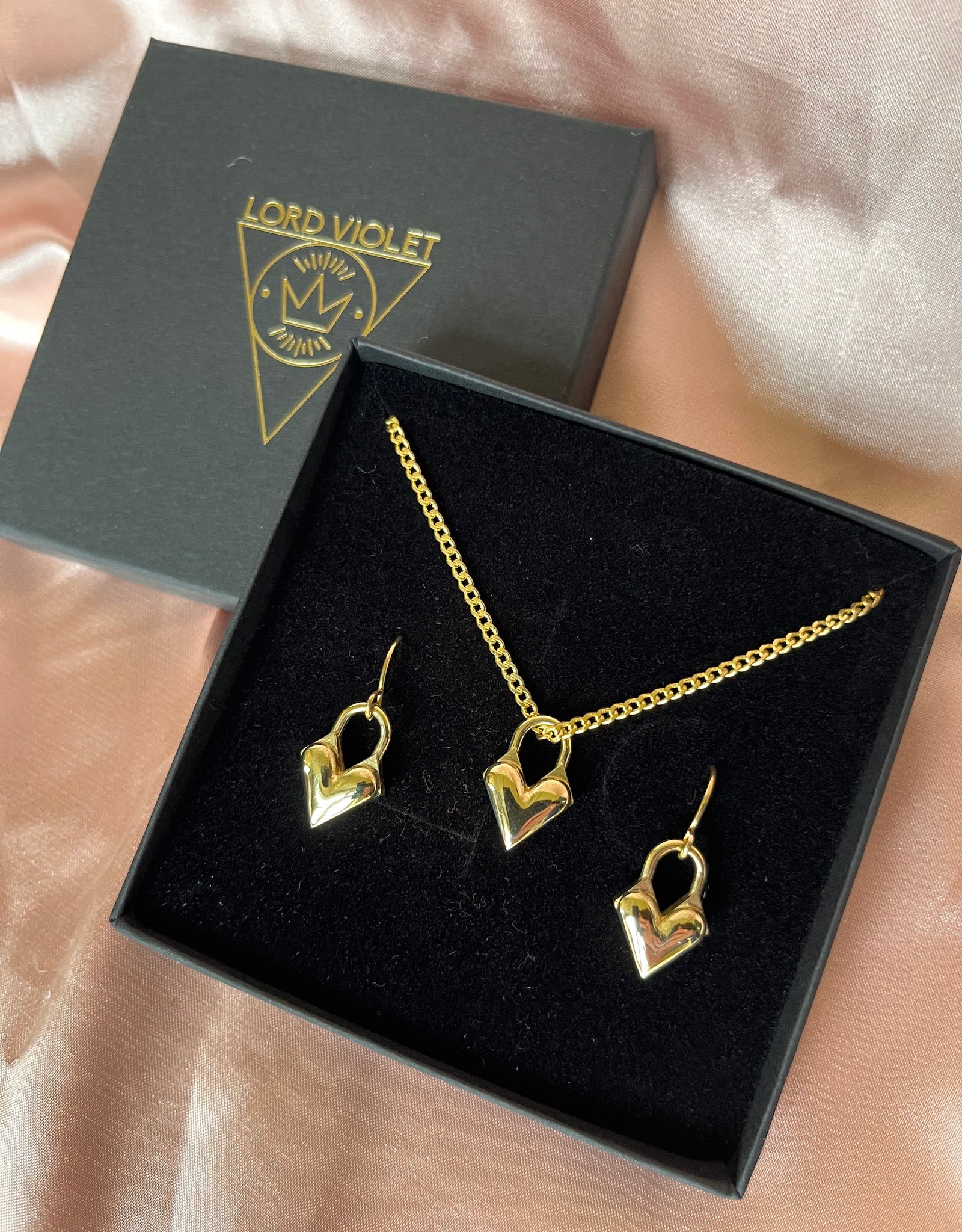 Gold jewelry gift set with necklace and earrings in a 'Lord Violet' box on a pink silk background