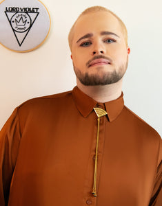 Model wearing gold fan bolo tie on a foxtail chain and bronze silk collared shirt