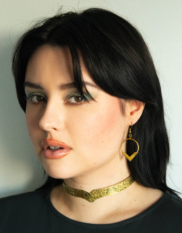 Model wearing gold choker with floral pattern and gold pointed hoop earrings