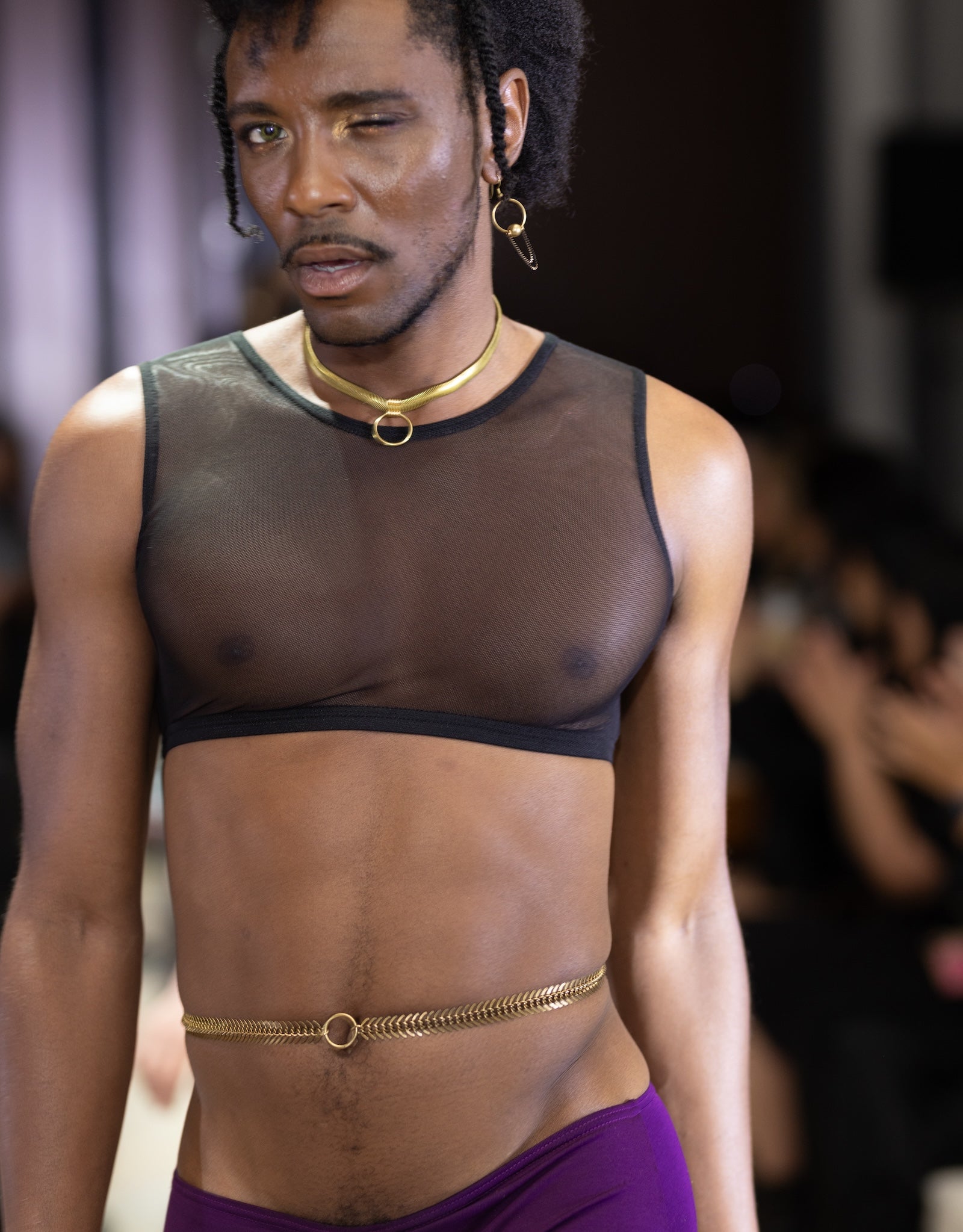 Model on runway wearing gold belly chain and black mesh crop top