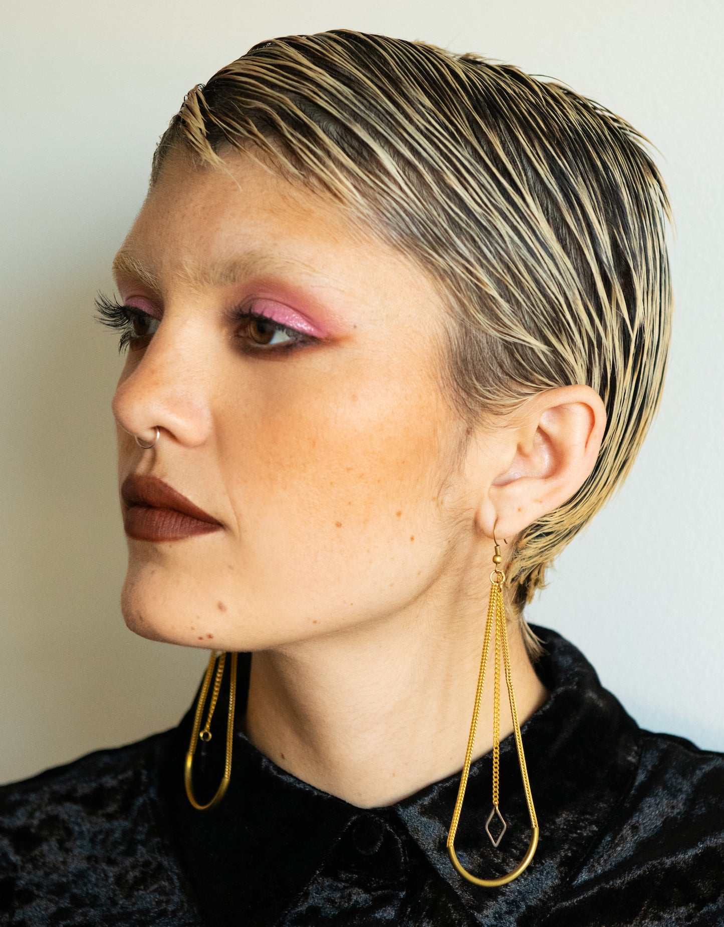 Side view of model wearing long arch earrings with triangle charms and black velvet button up shirt