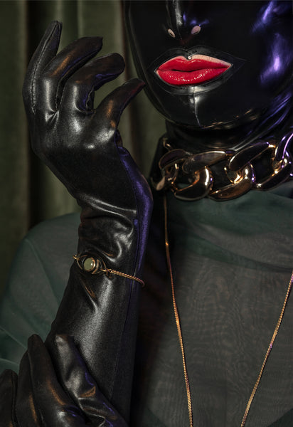 Model wearing gold eye bracelet, black gloves and a black latex mask