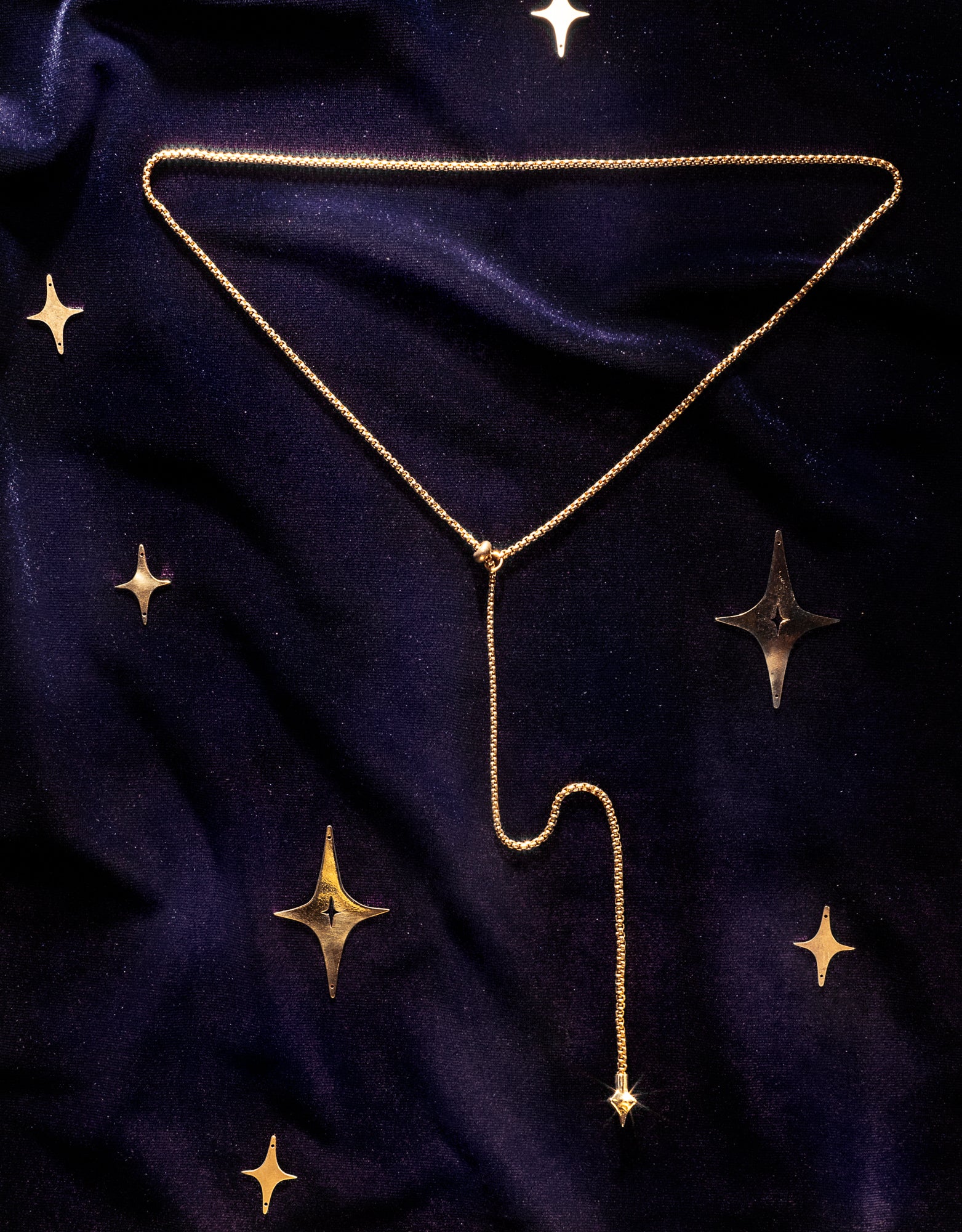 A delicate gold Y-shaped necklace with a long drop chain, on a dark navy blue velvet fabric decorated with gold stars.