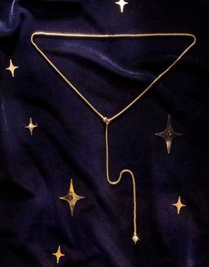 A delicate gold Y-shaped necklace with a long drop chain, on a dark navy blue velvet fabric decorated with gold stars.