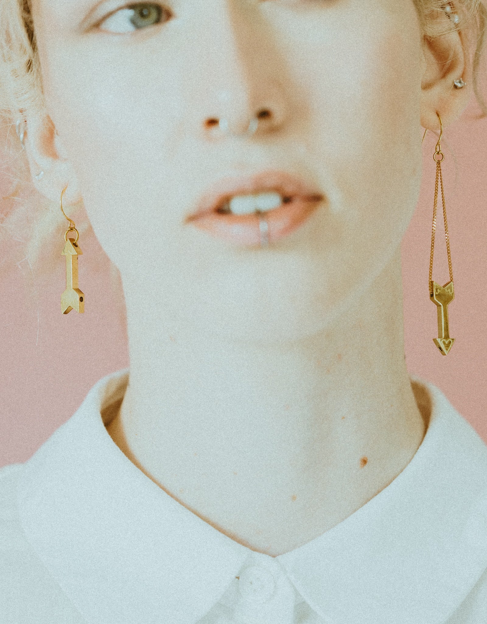 Close-up of model wearing gold heart charm earrings and white button up shirt