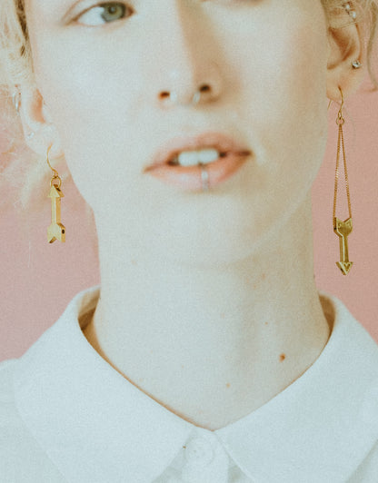 Close-up of model wearing gold heart charm earrings and white button up shirt