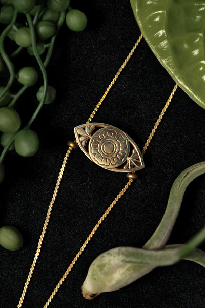 Close-up of gold flower bolo tie pendant on a black background, surrounded by plants