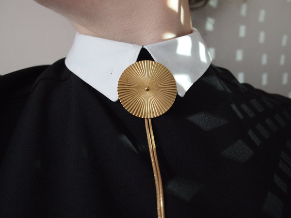 Close up of gold ridged bolo tie on model wearing a collared shirt