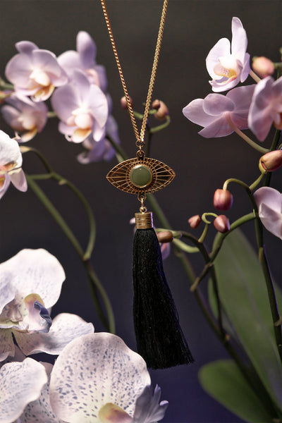 Resin eye pendant and black tassel of long gold necklace, surrounded by orchids