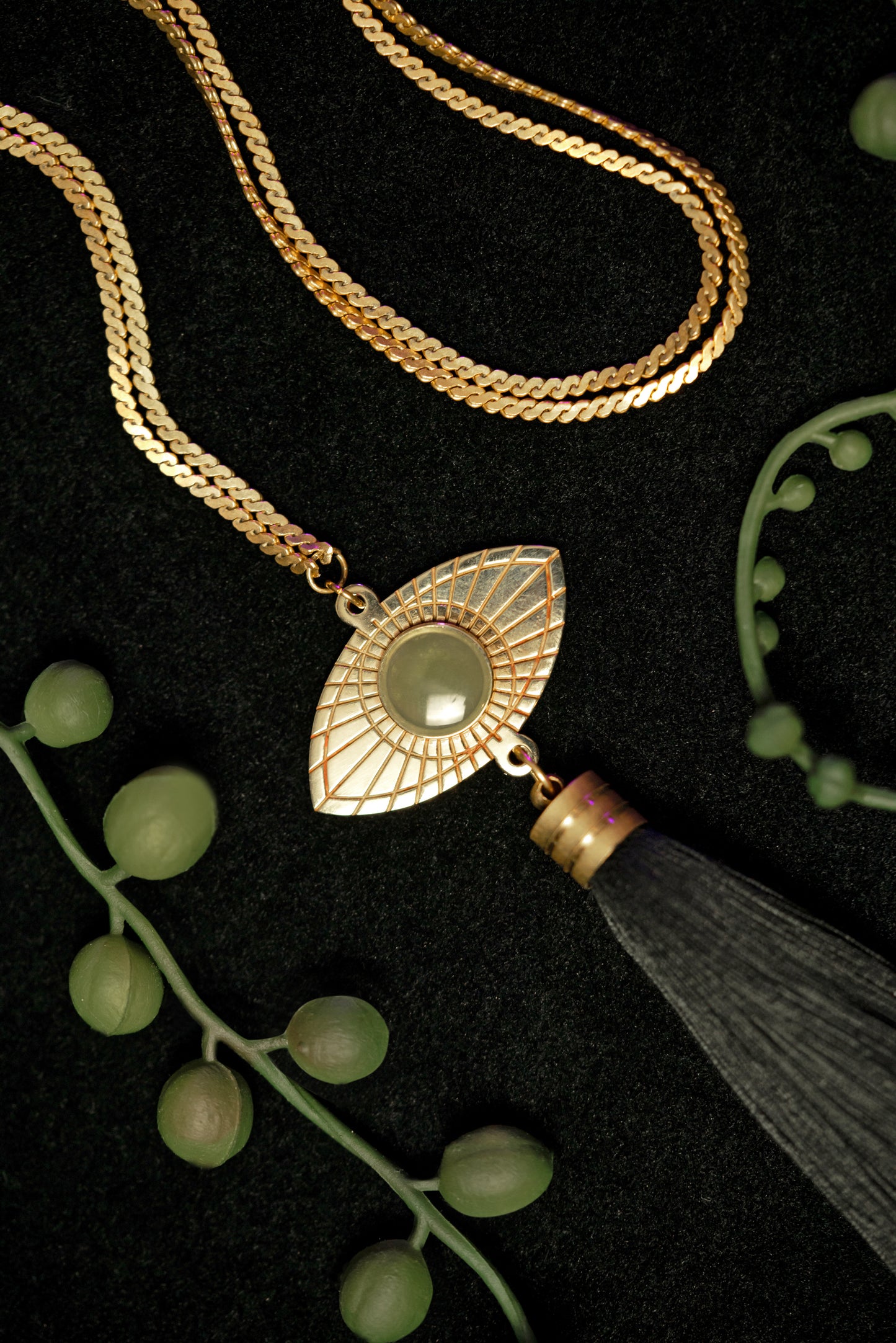 Close-up of gold eye pendant of long tassel necklace, surrounded by string of pearl plant