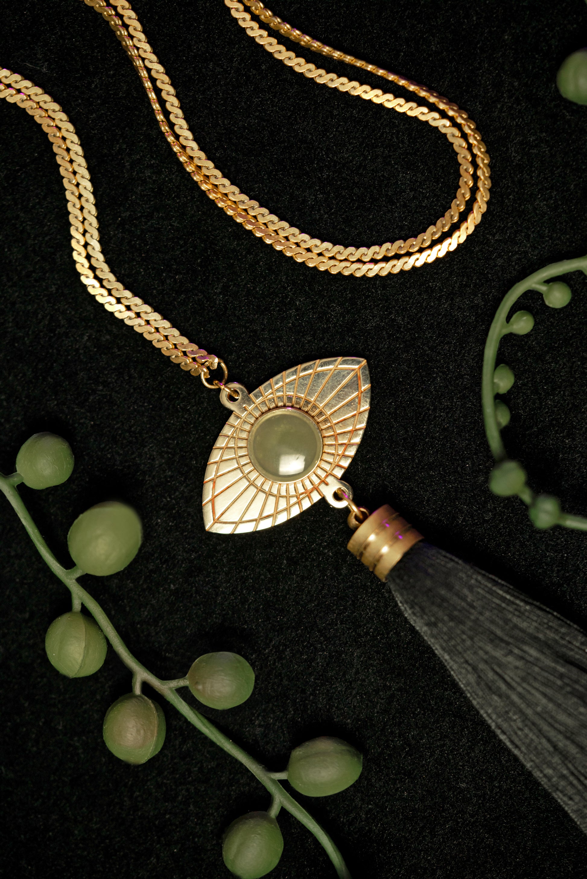 Close-up of gold eye pendant of long tassel necklace, surrounded by string of pearl plant