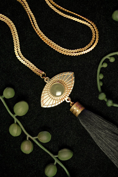 Close-up of gold eye pendant of long tassel necklace, surrounded by string of pearl plant