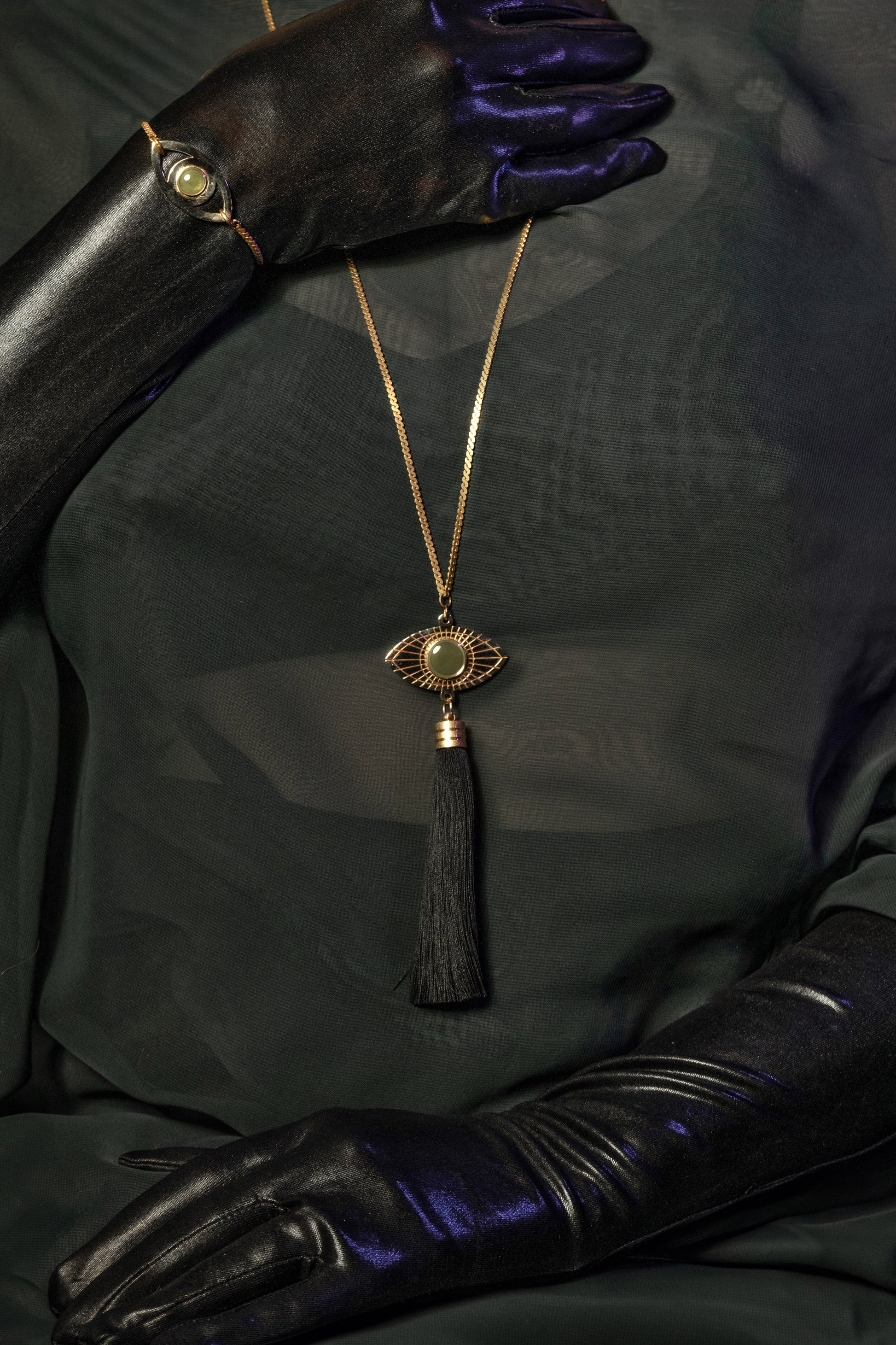 Gold eye pendant necklace on a model wearing sheer green top and black gloves