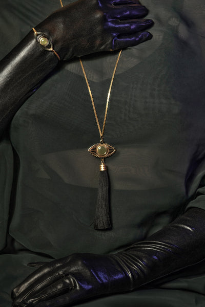 Gold eye pendant necklace on a model wearing sheer green top and black gloves