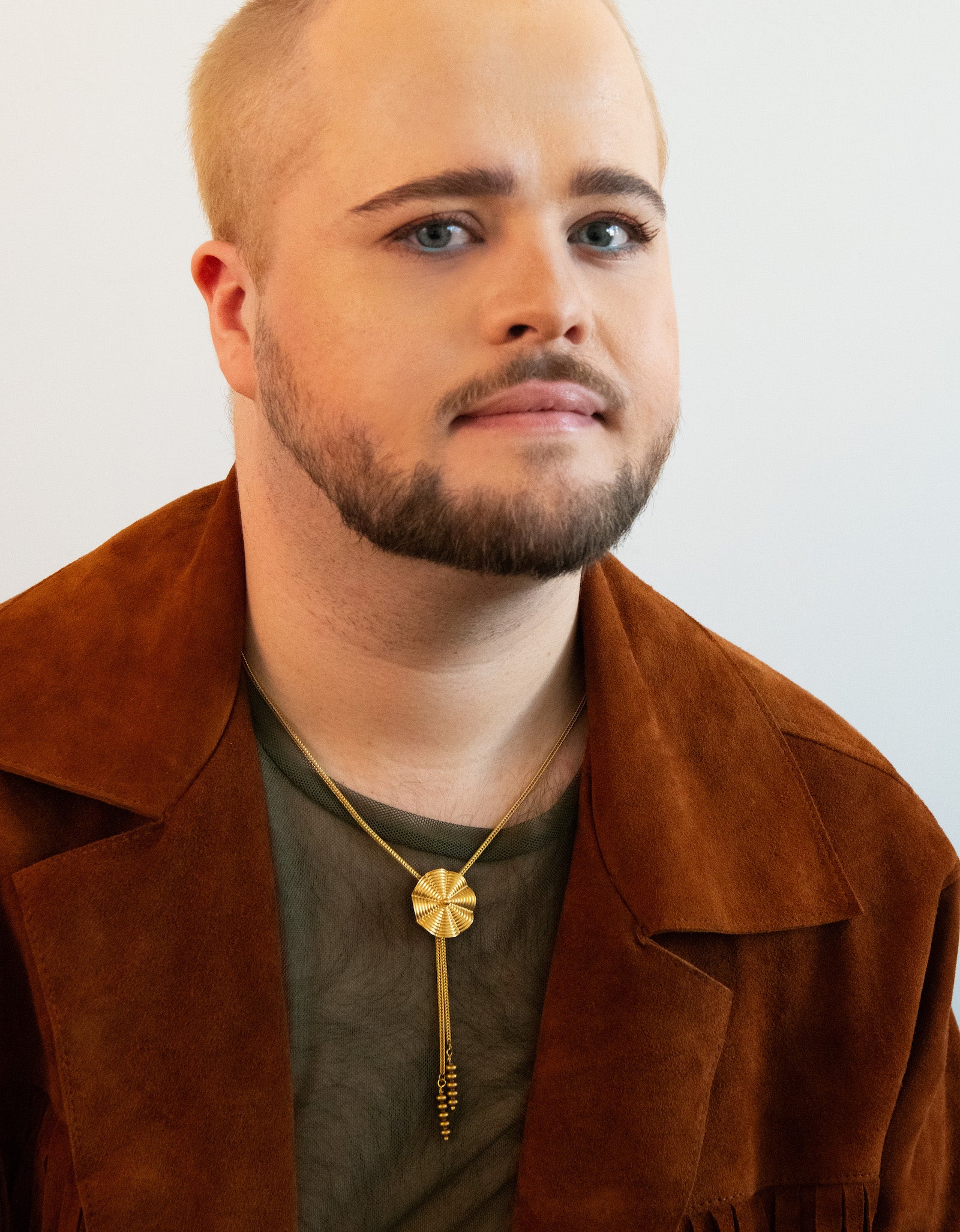 Model wearing wavy pendant bolo tie, green mesh shirt and tan jacket